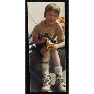 A boy sits on the curb with a drink during the Battle of Bunker Hill Road Race