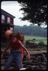 Eben Light and Sequoyah Frey (in face paint) playing on stone wall in front of the house, Montague Farm Commune