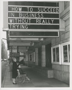 Mrs. Frances Marsala seated in her wheelchair with a friend or attendant outside a theater