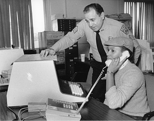 Unidentified woman at desk on phone with a Boston Police sergeant looking at computer screen