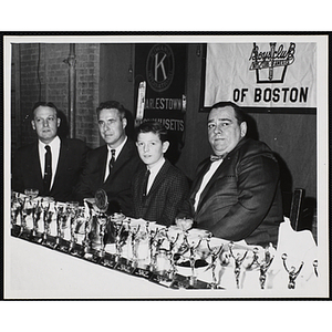 William J. Lynch, on the far left, seated at a table with many small trophies alongside two other men and a boy at a Charlestown Kiwanis Club event