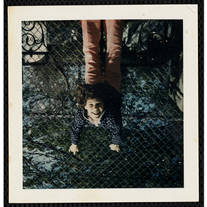A girl from the South Boston Boys' Club hanging from a chain link fence with her head upside down