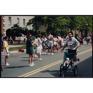 A man pushes a baby in a stroller as he runs in the Battle of Bunker Hill Road Race