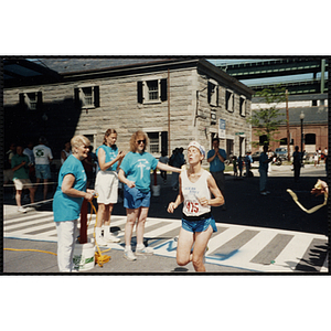 A runners crosses the finish line, breaking the tape held for her by race officials during the Battle of Bunker Hill Road Race