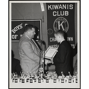 A man presents a certificate to a boy and shakes his hand at a Kiwanis Club's awards ceremony