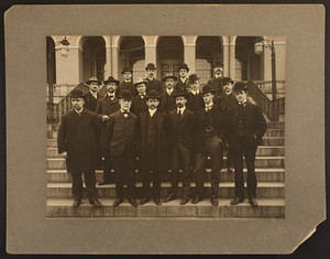 Group portrait of sixteen newspaper men and reporters standing on the front steps of the Massachusetts State House