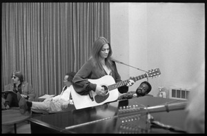 Judy Collins playing guitar by a piano (Michael Sahl in background, center)