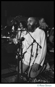 Ram Dass kneeling at the microphone, addressing the audience at the Winterland Ballroom during his 'marathon'