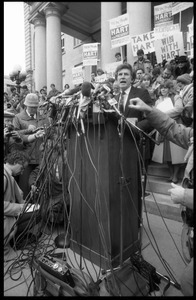 Gary Hart at a microphone-encrusted podium, addressing an crowd after renewing his bid for the Democratic nomination for the presidency