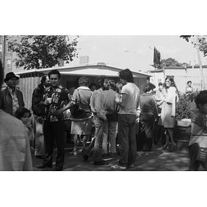 People congregate near a food vending stand at a Latino street festival; they are drinking, talking, walking, standing, or waiting in line for food