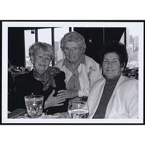 Two women seated at a table, another woman stands behind them for a picture at a St. Patrick's Day Luncheon