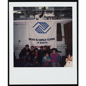 Nine boys and girls posing in front of the Boys and Girls Clubs of Boston banner while a girl, facing away from the camera, looks on during an event at the Chelsea Clubhouse