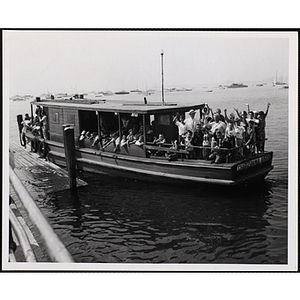 A group of boys with the Boston Rotary Club's Les Rowding and Edward Rowe Snow wave at the camera from a boat in Boston Harbor
