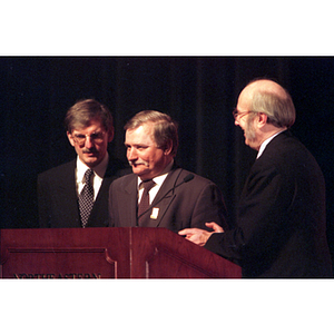 Lech Walesa stands at the podium with two men at the inauguration of the International Degree Program