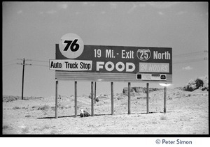 Cow sitting in the shade beneath a billboard: '76 auto truck stop food, Exit 25 North'