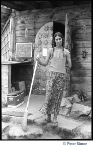 Young woman with a broom standing near a sign for Sufi dancing, Lama Foundation