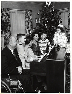 Mayor John F. Collins, Mary Collins, and their children, Thomas, Patricia, John, and Margaret, gathering around a piano in front of a Christmas tree