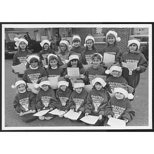 Group of children posing together, dressed in Santa Claus hats and Eastern Middlesex Family Young Men's Christian Association shirts