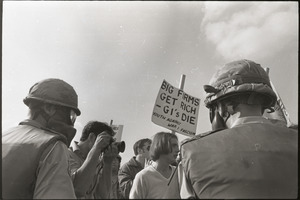 Antiwar demonstration at Fort Dix, N.J.: military police with gas masks facing protesters carrying sign reading "Big firms get rich -- GI's die"