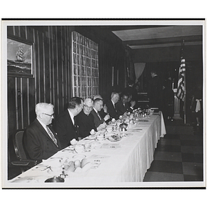 Eight men, seated at a long table, eat and converse at the Kiwanis Club's Bunker Hill Postage Stamp Luncheon