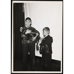 A boy holds a turkey and looks at the camera while another boy, facing left, displays a piece of paper during a Boys' Club event