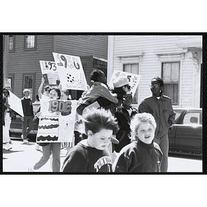 A female staff member with a girl on her back walking with several other girls holding up their signs during the Boys and Girls Clubs of Boston 100th Anniversary Celebration Parade