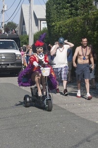 Parade marcher in a feathery costume on a scooter, with a megaphone : Provincetown Carnival parade