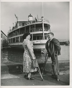 Woman and man with crutches stand before boat