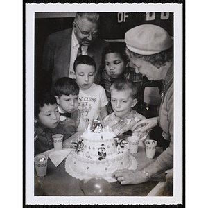 Five boys blow on candles on a cake as a woman and man look on