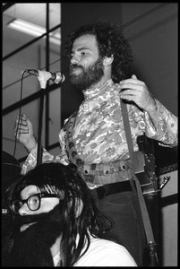 Jerry Rubin, with bandolier and toy assault rifle slung over his shoulder, addressing the audience at the microphone