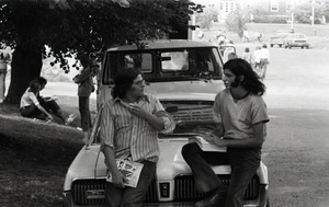Bill Grabin, with pile of Free Spirit Press magazine, talking with UMass Amherst student sitting on the hood of a 1968 Mercury Cougar
