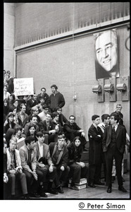 Audience awaiting speech by presidential candidate Eugene McCarthy at Boston University, standing under large poster for McCarthy