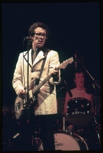 Elvis Costello and the Attractions in concert: Costello on guitar (drummer Bruce Thomas in background)