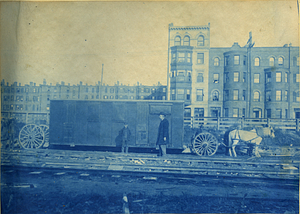 [Man and boy in front of a portable office being moved by a horse and carriage]