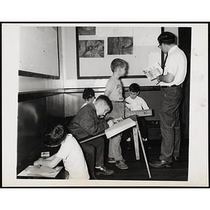 An art instructor and a boy stand together looking at a drawing while four others work on their projects at the Charlestown Boys' Club