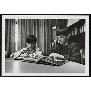 Two boys read books at a table in a library