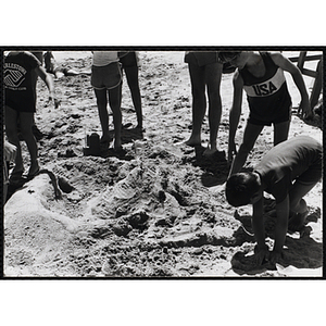 A group of boys work on a sandcastle on a beach