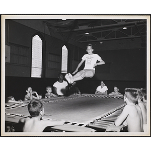 A group of boys around a trampoline watch a boy bounce in the air