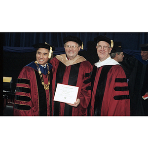 Neal Finnegan holds his honorary degree as he poses with President Freeland and George Matthews