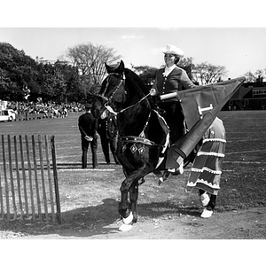 A woman rides a horse and waves a flag during a homecoming parade