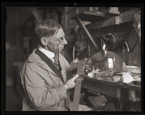 Walter G. Wolfe, industrial lens maker, at his work bench, measuring a lens