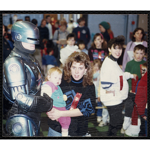 A woman with "DRUG FREE AND PROUD TO BE" ribbon holding a baby girl and posing with a man in a RoboCop suit at a joint Charlestown Boys and Girls Club and Charlestown Against Drugs (CHAD) event