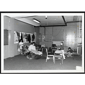 Boys and Girls Club members sit and stand in a room with a television, a couch, and several chairs