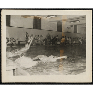 Teenage boys begin a backstroke race in a natorium pool as spectators look on
