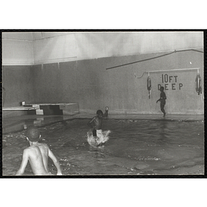 A boy enters the water from a diving board in a natorium pool