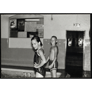 A girl and boy stand at the edge of a natorium pool