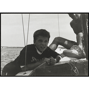 A boy hangs off the side of the sailboat as man looks on in Boston Harbor