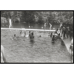 A group of boys stand on a dock while children splash in the water