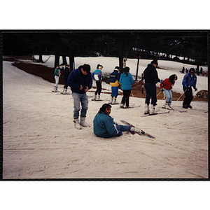 A girl sits in snow with skis and poles as a man looks on during an outing to Nashoba Valley