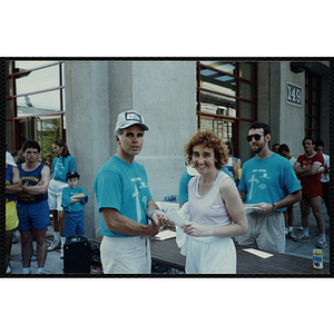 A man and a woman shake hands as they hold a certificate at the Battle of Bunker Hill Road Race